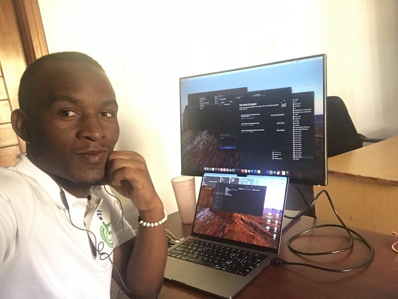At a desk with a large monitor showing code and a laptop alongside