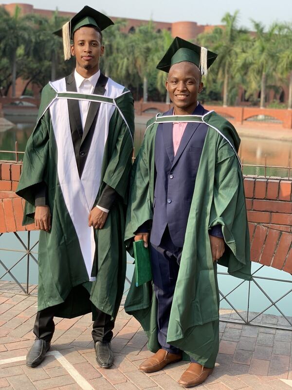 Two graduates in academic gowns standing together outdoors