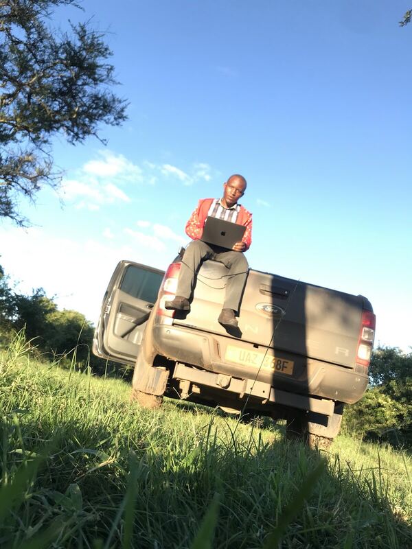 Sitting on the back of a pickup truck outdoors, working on a laptop