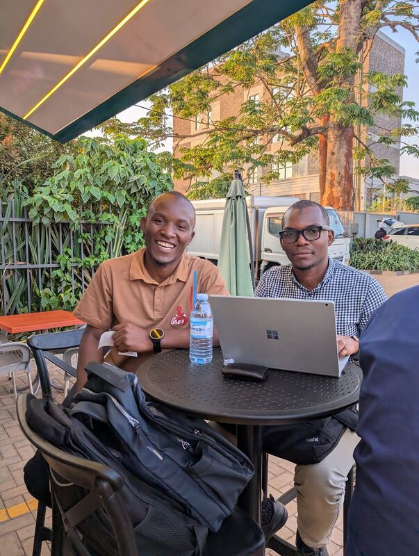 Two people at an outdoor table with a laptop between them, in discussion