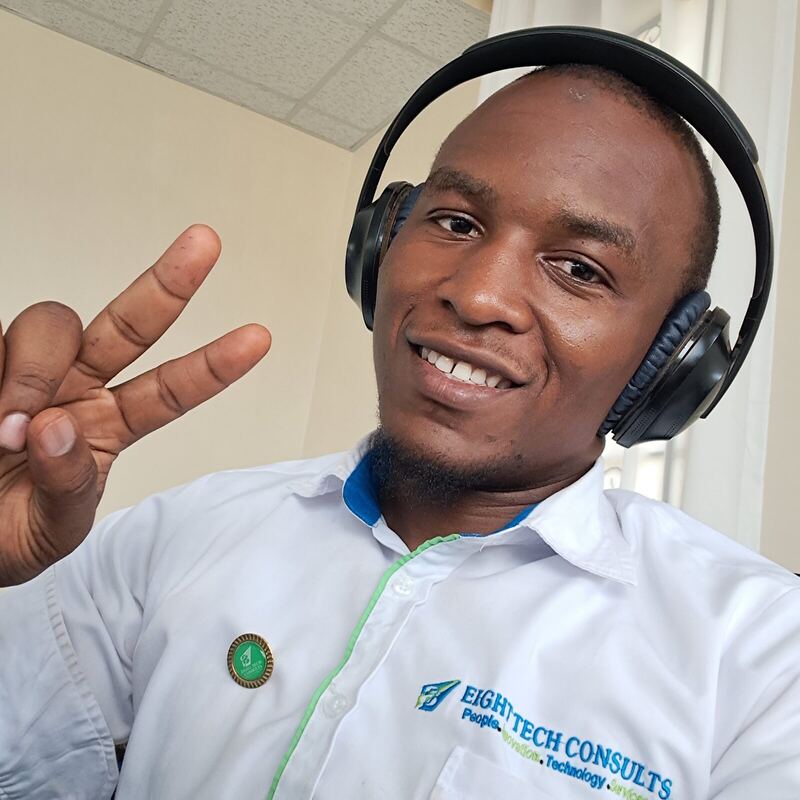 Smiling at the camera wearing headphones and a branded work shirt