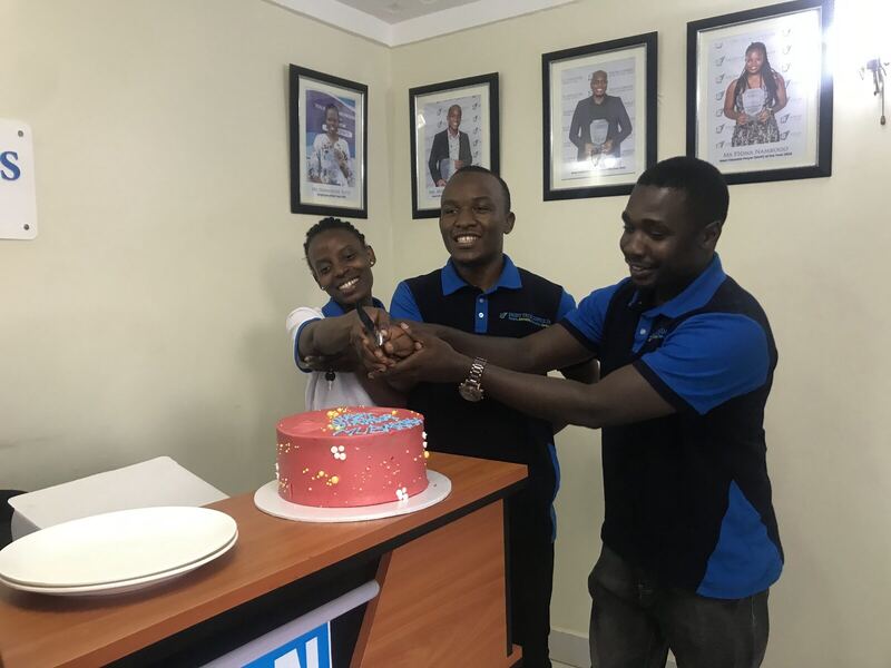 Three colleagues around a cake in an office, celebrating together