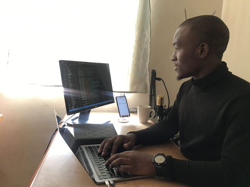 Working at a desk with a monitor of code, a laptop and a microphone