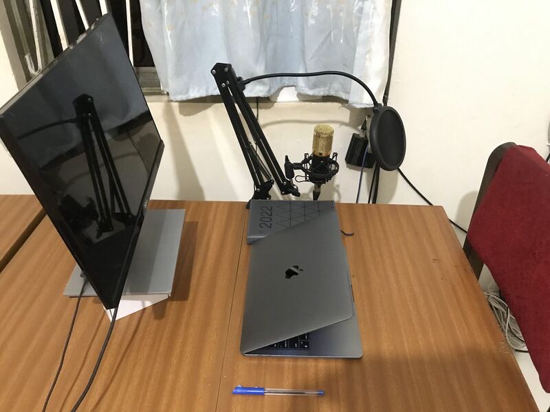 A desk holding a closed laptop, an external monitor and a studio microphone